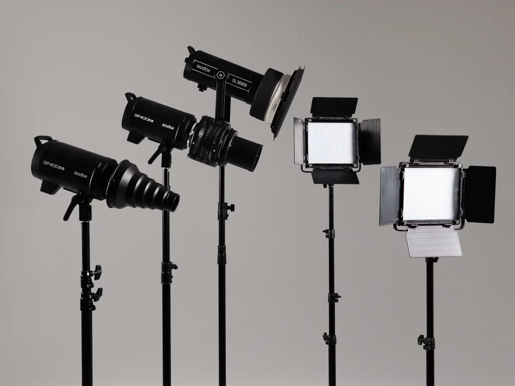 Drei Studiolampen und zwei LED‑Panels mit Barn Doors auf Lampenstativen vor neutralem Hintergrund.